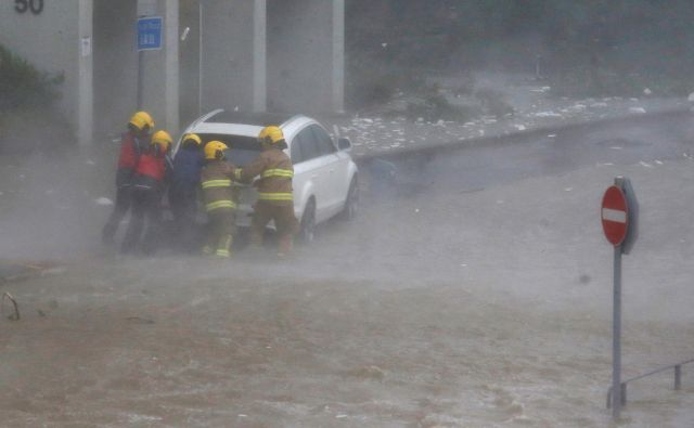 Gasilci pomagajo v poplavah ujetemu vozniku. FOTO: Bobby Yip/Reuters