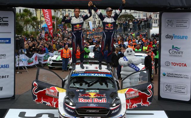 Sebastien Ogier in njegov sovoznik Julien Ingrassia sta se takole na strehi svojega forda veselila četrte letošnje zmage v svetovnem prvenstvu. FOTO: Geoff Caddick/AFP