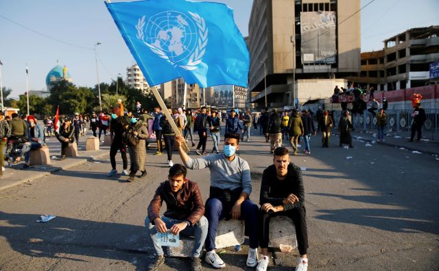 Udeleženec protestov v Iraku z zastavo Združenih narodov. FOTO: Thaier Al-sudani/Reuters