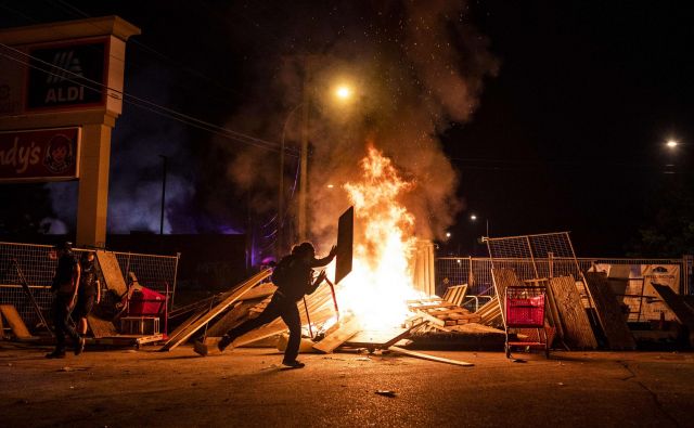 Protestnik pred zažgano trgovino v Minneapolisu Foto AFP