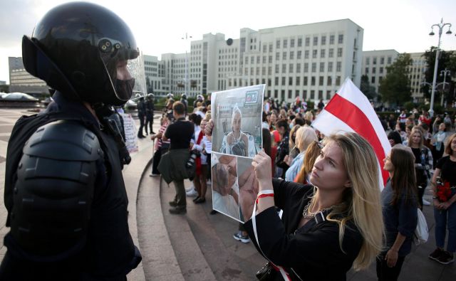 Protestniki zahtevajo razveljavitev volitev in odstop predsednika. Protestnica na sliki policistu kaže fotografijo protetsnice, ki so jo poškodovale varnostne sile. FOTO: izroček Via Reuters