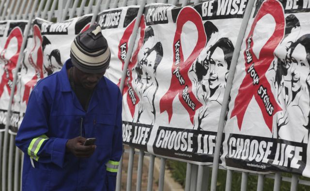 FILE -- In this Dec. 1, 2014 file photo a man makes a call on a mobile phone as he passes  a World AIDS Day banners on the perimeter of an office building in Sandton, Johannesburg, South Africa. A new vaccine against HIV, to be tested in a trial to be